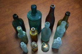 The glass bottles are pressed from a mold. The iridescent colors are a symptom of “glass disease,” which was caused by prolonged exposure to water under the ground.