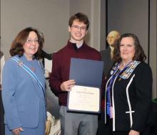 Boy poses with an award and two middle-aged women in blue