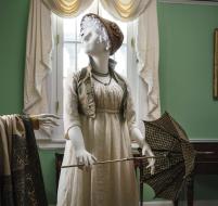 A changeable silk taffeta vest with silk cord trim and buttons, a braided straw hat with silk satin ribbon and a parasol with woven checked cotton, metal frame, ivory handle and tip.