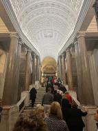 The group walks up stairs under a decorative white ceiling within the Vatican.